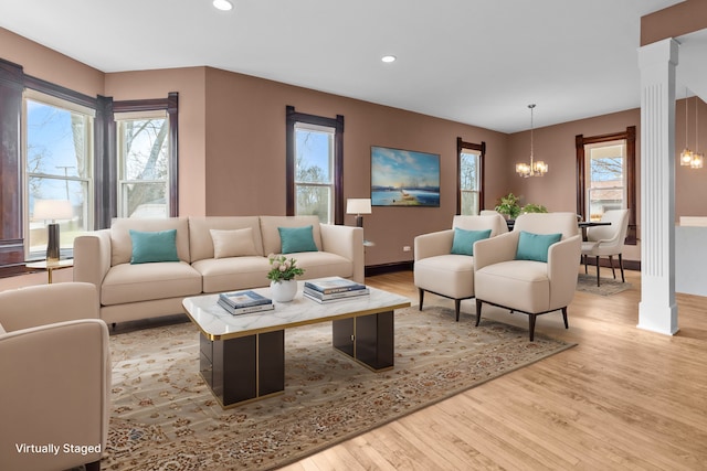 living room featuring decorative columns, light wood-type flooring, and an inviting chandelier