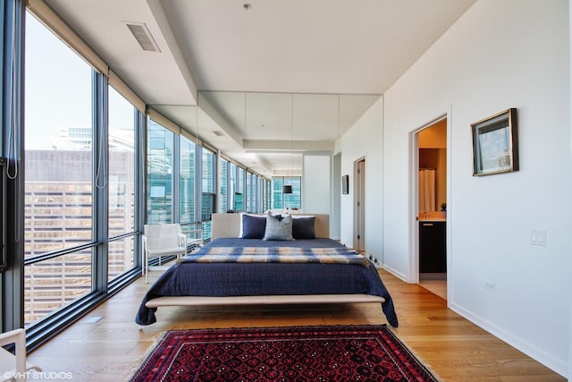 bedroom featuring expansive windows, ensuite bath, and light hardwood / wood-style flooring