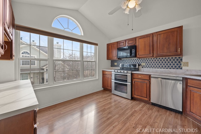 kitchen featuring appliances with stainless steel finishes, tasteful backsplash, lofted ceiling, ceiling fan, and light hardwood / wood-style flooring