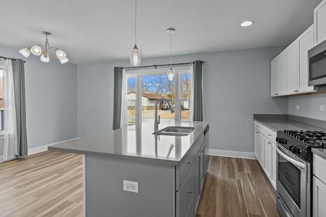 kitchen featuring pendant lighting, sink, white cabinets, stainless steel appliances, and a center island with sink