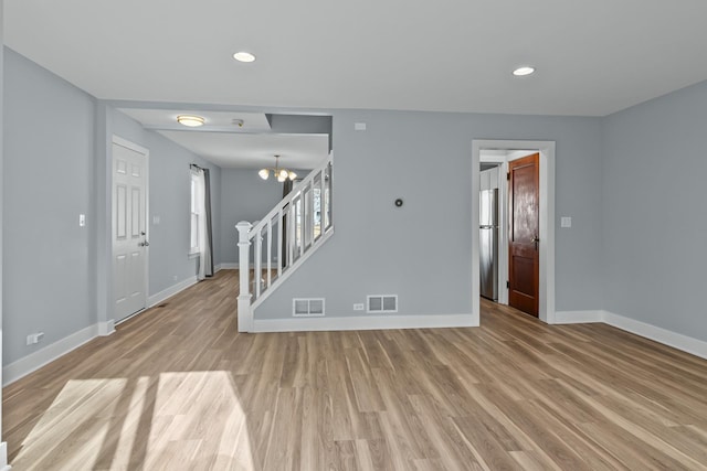 unfurnished living room featuring a chandelier and light wood-type flooring