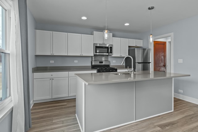 kitchen featuring hanging light fixtures, stainless steel appliances, white cabinets, and a center island with sink