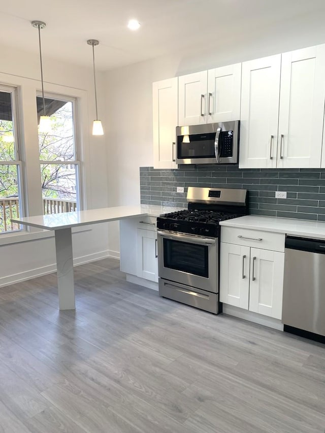 kitchen with stainless steel appliances, white cabinets, and decorative light fixtures