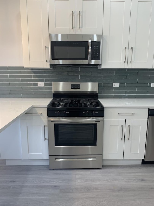 kitchen with tasteful backsplash, stainless steel appliances, white cabinets, and light wood-type flooring