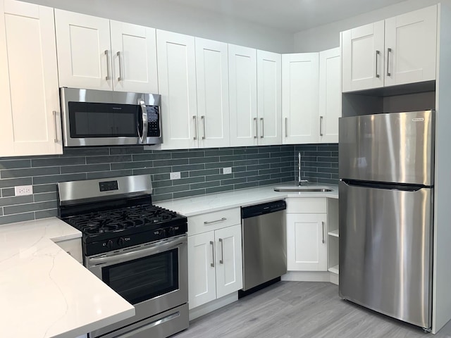 kitchen featuring appliances with stainless steel finishes, tasteful backsplash, white cabinetry, sink, and light stone countertops