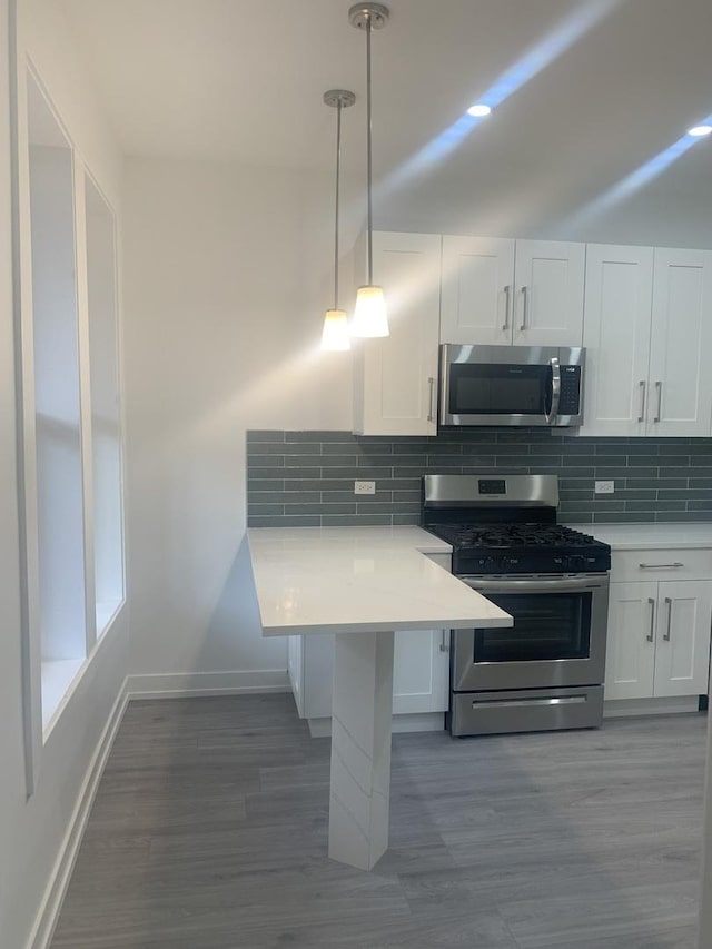 kitchen featuring tasteful backsplash, white cabinetry, appliances with stainless steel finishes, and pendant lighting