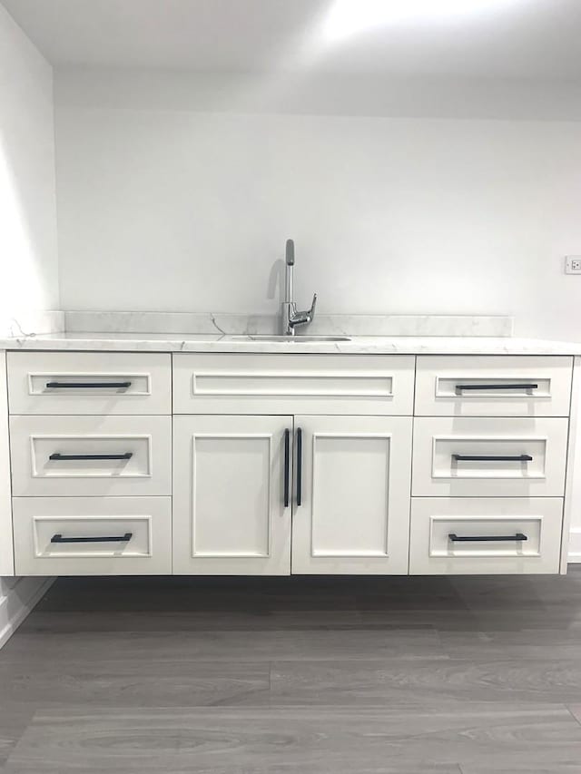 bar featuring light stone countertops, sink, white cabinets, and dark hardwood / wood-style floors