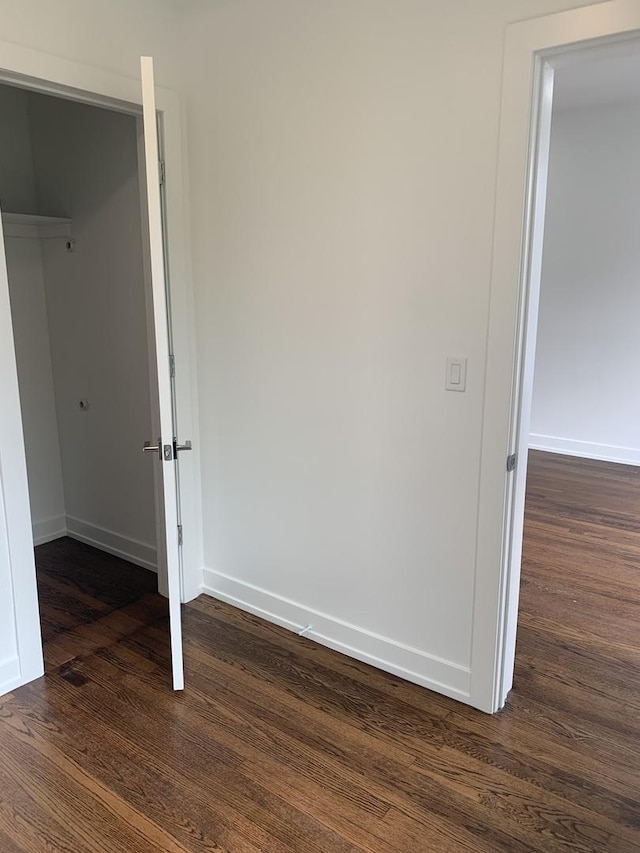 unfurnished bedroom with a spacious closet, dark wood-type flooring, and a closet