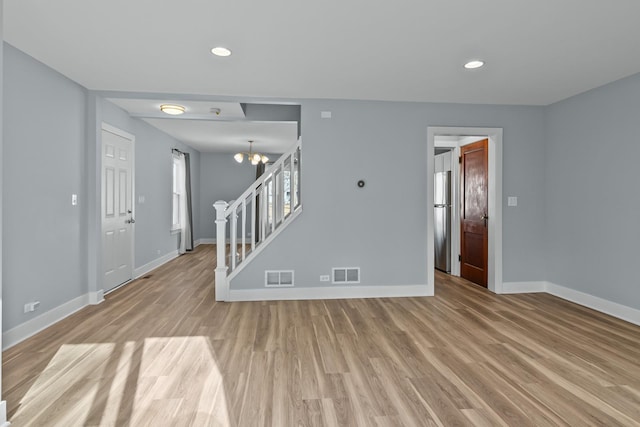 unfurnished living room with a notable chandelier and light wood-type flooring