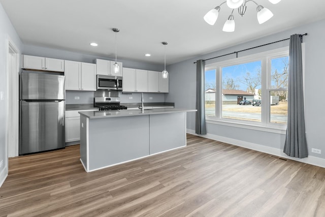 kitchen featuring an island with sink, wood-type flooring, white cabinets, hanging light fixtures, and stainless steel appliances