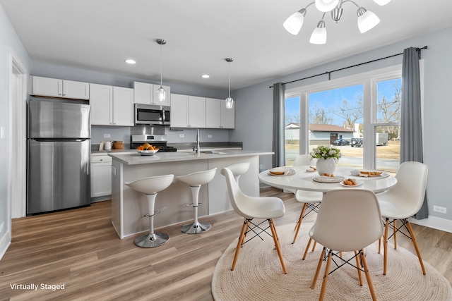 kitchen with appliances with stainless steel finishes, white cabinetry, hardwood / wood-style floors, a kitchen island with sink, and decorative light fixtures