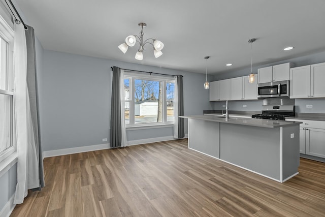 kitchen with a center island with sink, light wood-type flooring, hanging light fixtures, appliances with stainless steel finishes, and white cabinets