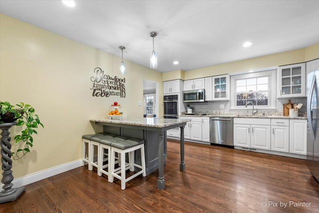 kitchen with appliances with stainless steel finishes, a breakfast bar, decorative light fixtures, white cabinets, and light stone counters