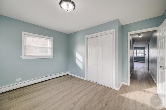 unfurnished bedroom featuring light hardwood / wood-style floors, a closet, and baseboard heating