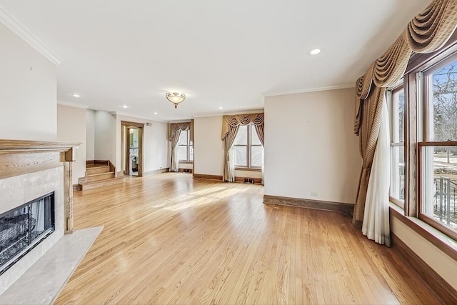 unfurnished living room featuring ornamental molding, a wealth of natural light, a high end fireplace, and light hardwood / wood-style floors