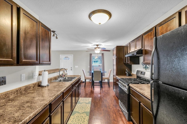 kitchen with dark wood-type flooring, sink, stainless steel gas range oven, a textured ceiling, and black refrigerator