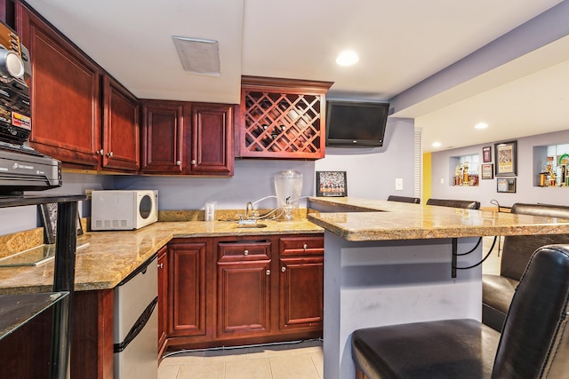 kitchen featuring stainless steel fridge, a kitchen bar, light stone counters, light tile patterned flooring, and kitchen peninsula