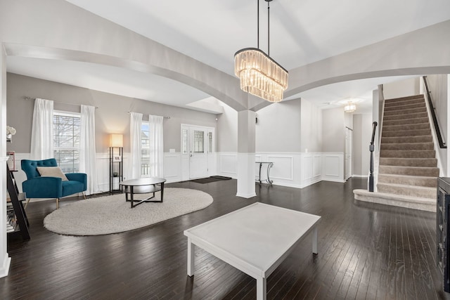 living area with arched walkways, dark wood-style flooring, a wainscoted wall, stairway, and a chandelier