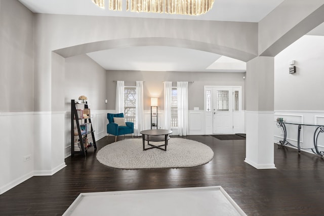 foyer with arched walkways, a wainscoted wall, a decorative wall, and wood finished floors