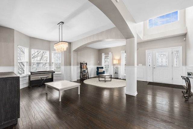 foyer with wood-type flooring, arched walkways, a notable chandelier, and wainscoting