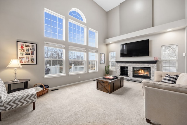 carpeted living area featuring visible vents, a fireplace, a towering ceiling, and baseboards