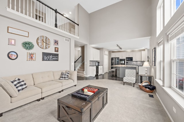 living room with a high ceiling, visible vents, baseboards, stairway, and dark colored carpet