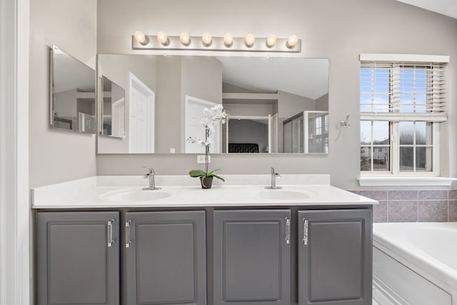 full bath with vaulted ceiling, a garden tub, a sink, and double vanity