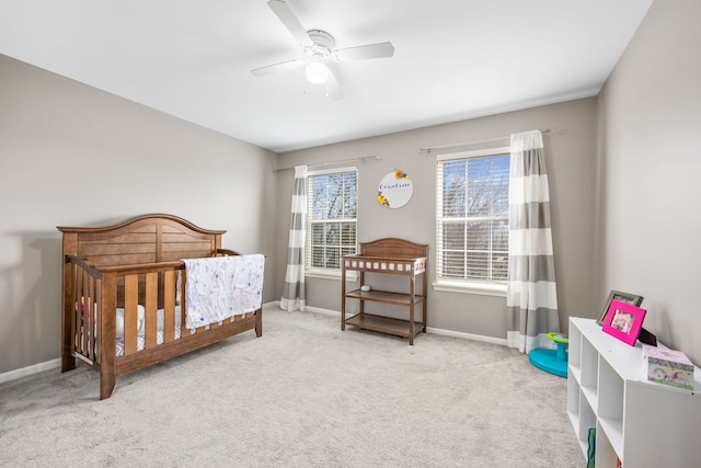 bedroom featuring carpet floors, a nursery area, baseboards, and a ceiling fan