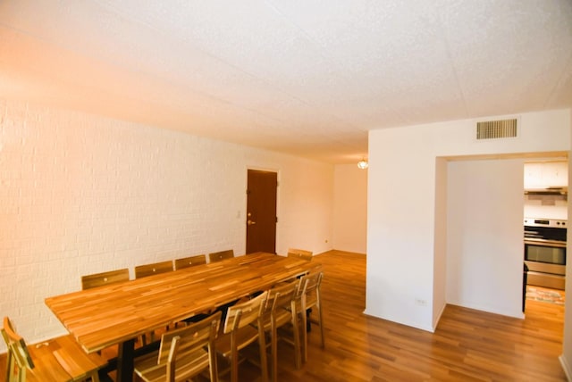 dining room featuring wood-type flooring and brick wall