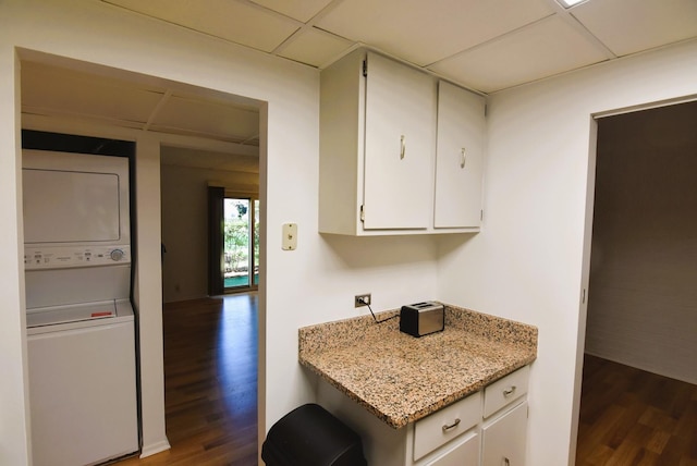 kitchen with dark hardwood / wood-style floors, a paneled ceiling, white cabinetry, stacked washer and clothes dryer, and light stone counters