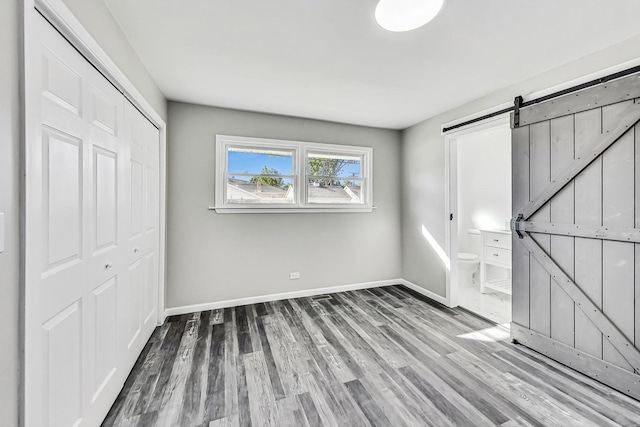 unfurnished bedroom featuring hardwood / wood-style flooring, ensuite bathroom, a barn door, and a closet