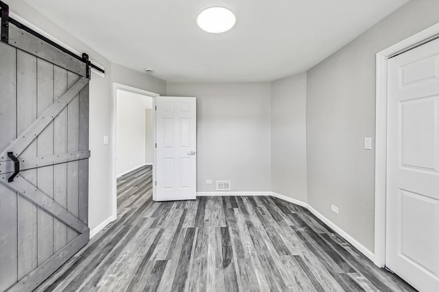 unfurnished bedroom featuring a barn door and dark wood-type flooring