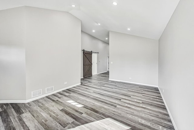 spare room featuring lofted ceiling, light hardwood / wood-style floors, and a barn door