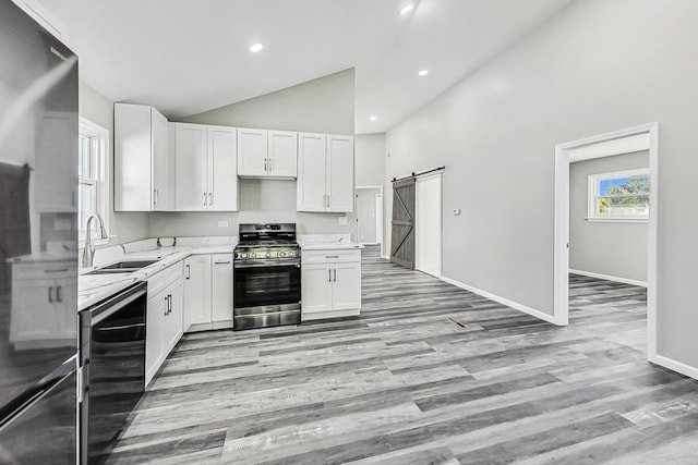 kitchen with white cabinetry, sink, light stone countertops, stainless steel gas range oven, and a barn door