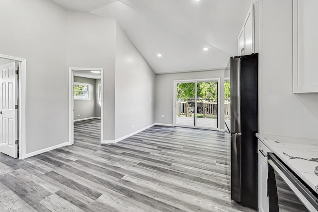 kitchen with lofted ceiling, light hardwood / wood-style flooring, black refrigerator, light stone countertops, and white cabinets