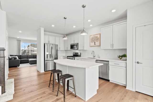 kitchen with appliances with stainless steel finishes, a kitchen island, white cabinetry, and decorative light fixtures