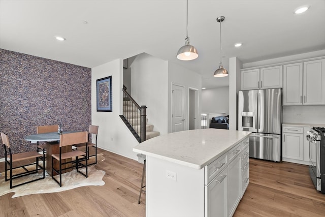 kitchen with a kitchen island, decorative light fixtures, light hardwood / wood-style floors, stainless steel appliances, and white cabinets