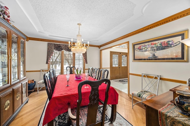 dining area featuring a raised ceiling, an inviting chandelier, a textured ceiling, and light wood-type flooring