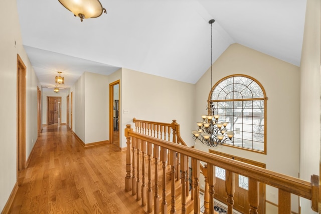 corridor featuring a notable chandelier, vaulted ceiling, and light hardwood / wood-style floors