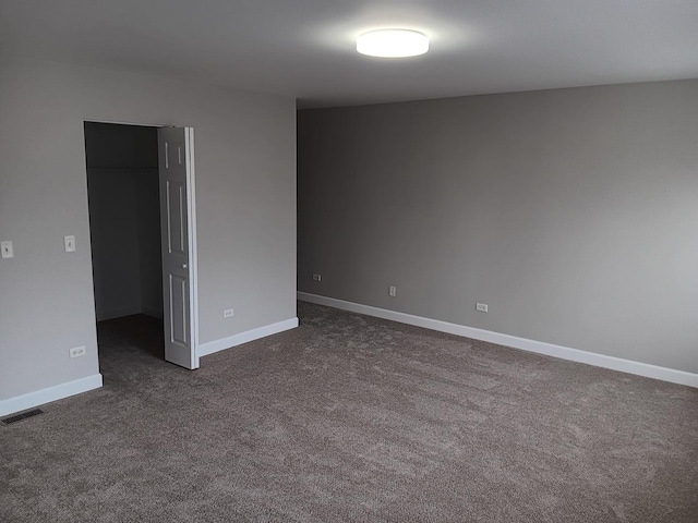 unfurnished bedroom with dark colored carpet, a walk in closet, and a closet