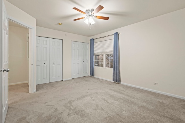 unfurnished bedroom featuring multiple closets, light colored carpet, and ceiling fan