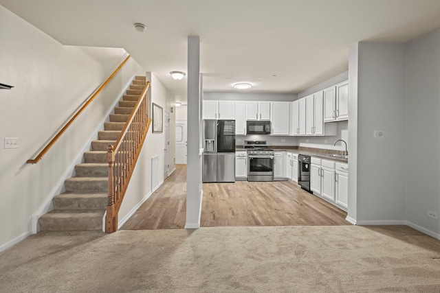 kitchen featuring light carpet, black appliances, and white cabinets