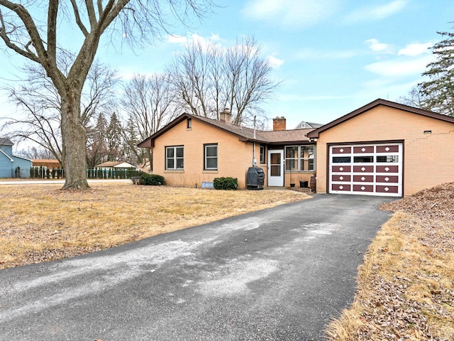 view of front facade featuring brick siding, a chimney, an attached garage, and aphalt driveway