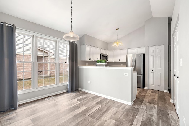 kitchen with appliances with stainless steel finishes, kitchen peninsula, pendant lighting, light hardwood / wood-style floors, and white cabinets