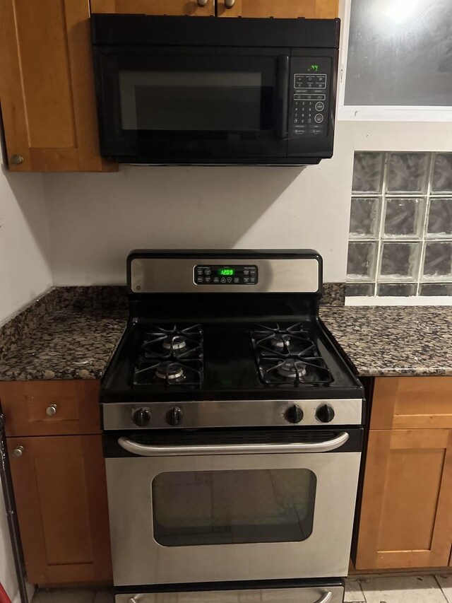 kitchen with stainless steel gas stove and dark stone counters