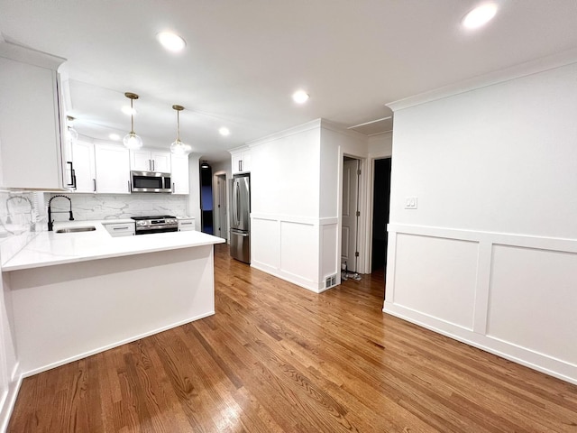 kitchen featuring pendant lighting, sink, white cabinetry, stainless steel appliances, and kitchen peninsula