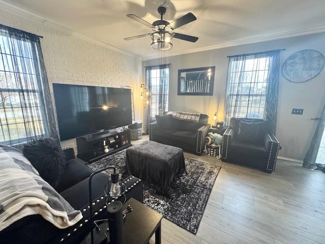 living room featuring crown molding, brick wall, a wealth of natural light, and light hardwood / wood-style flooring