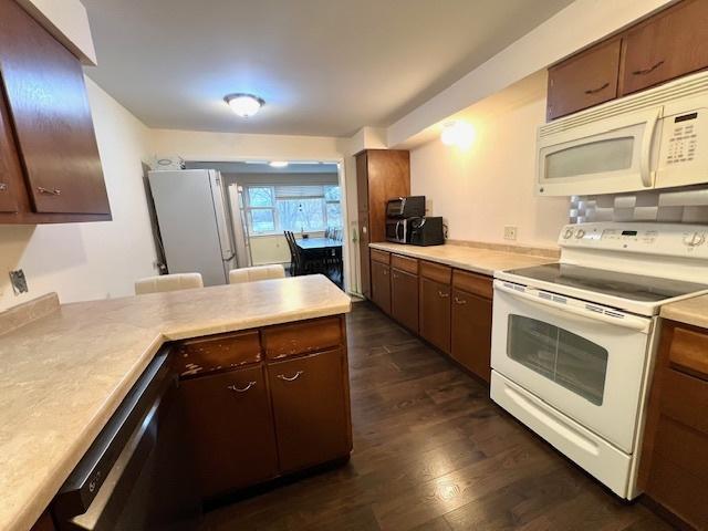 kitchen with light countertops, white appliances, dark wood-type flooring, and a peninsula