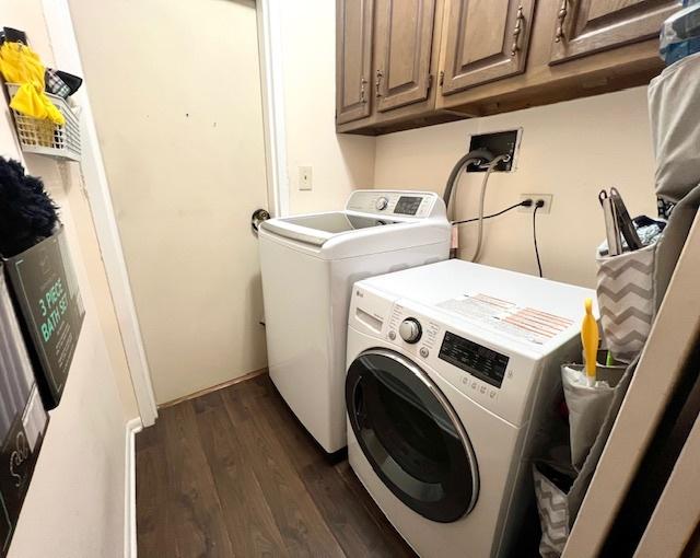 clothes washing area with dark wood-style floors, washer and dryer, and cabinet space