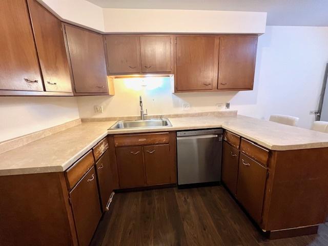 kitchen with dark wood-style floors, light countertops, stainless steel dishwasher, a sink, and a peninsula